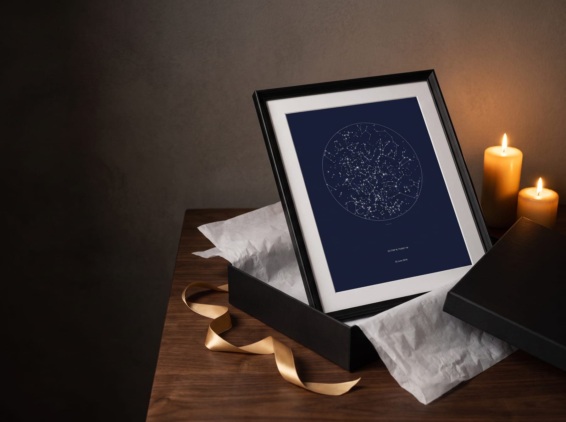 A star chart print in a black frame, lifted from its gift box beside two candles